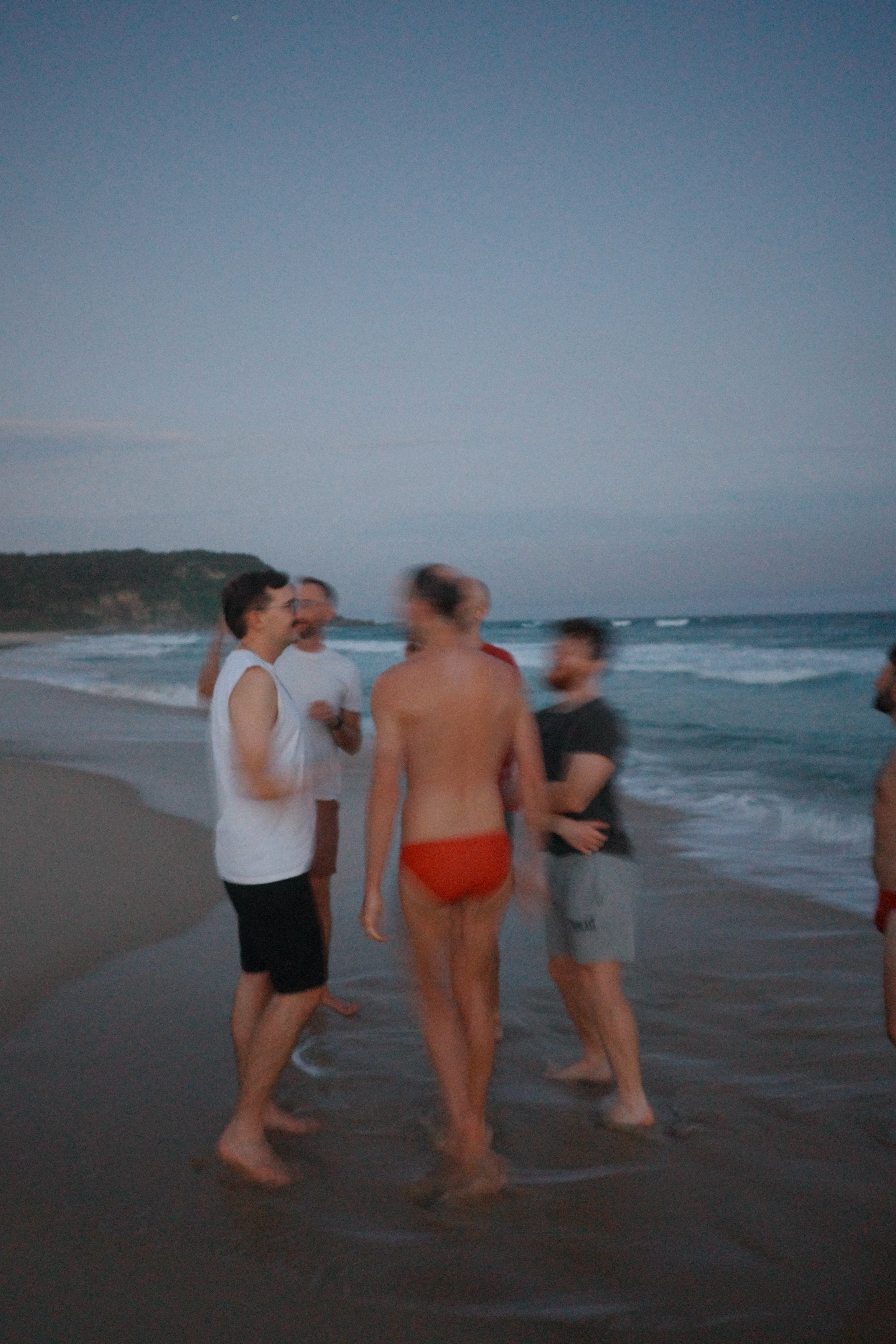 Group of friends standing in the shallows at dusk with motion blur, coastal headland in the background